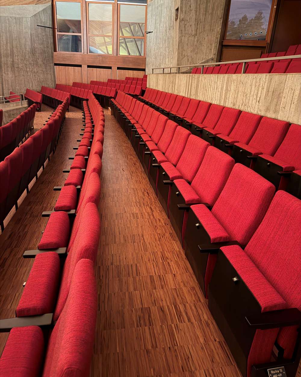 Rote Theaterbestuhlung in gestuften Reihen in einem Saal mit Holzverkleidung und Sichtbeton